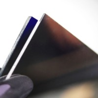 Optical Grade First Surface Mirror Acrylic wth protective laminate pulled back exposing front surface of mirror.Pictured are two samples.One at at quarter inch thickness and the other at an eighth of an inch thickness. acrylic-first-surface-mirror-thicknesses-available